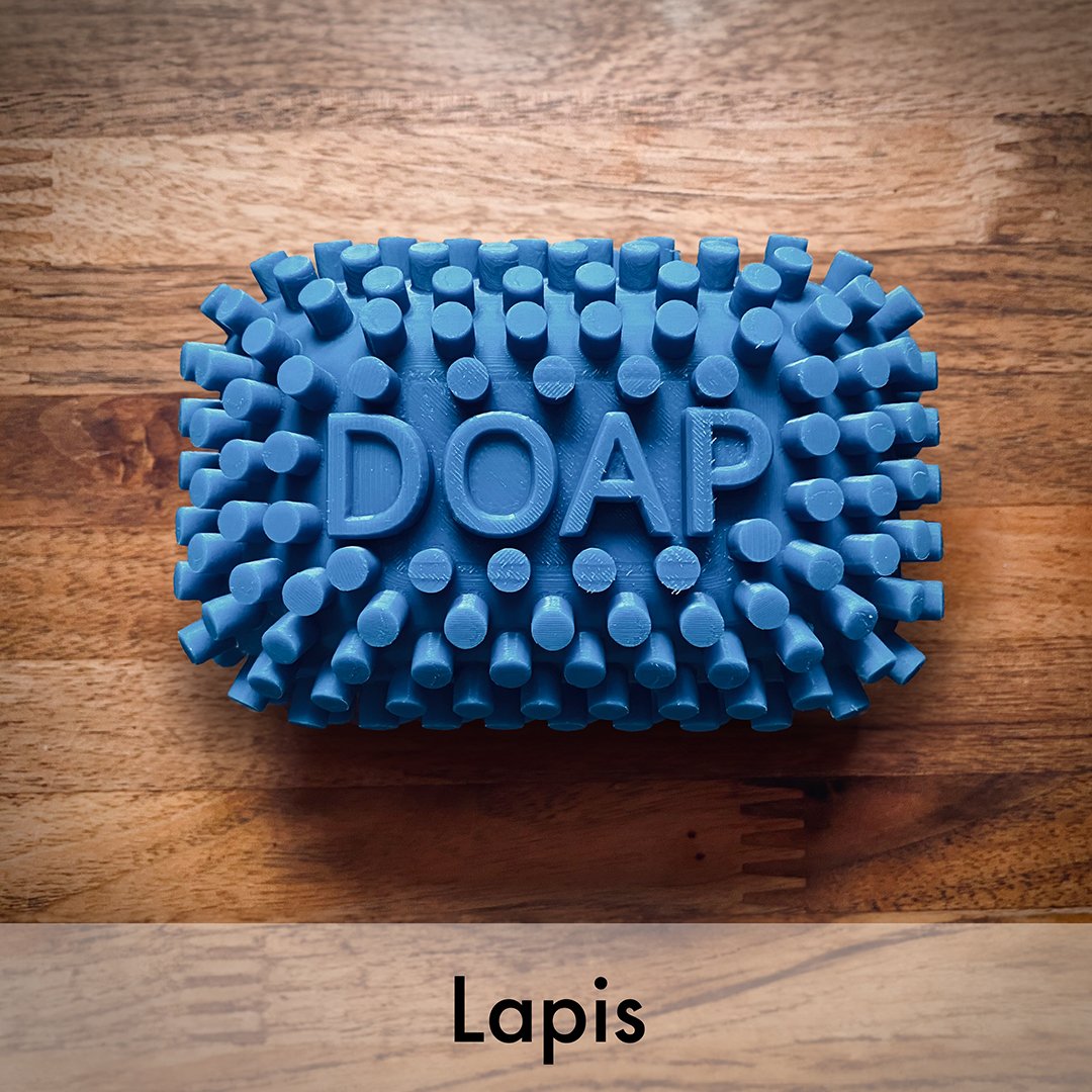 A textured dark blue DOAP silicone dough scrub barbar embossed with the brand name 'DOAP' and labeled 'Lapis' at the bottom, displayed on a wooden surface.